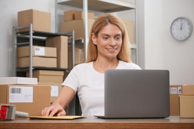 Photo of Seller with parcels and laptop in office. Online store