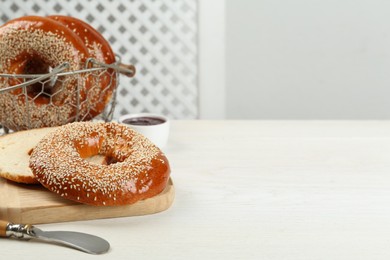 Delicious fresh bagels with sesame seeds on white wooden table, space for text