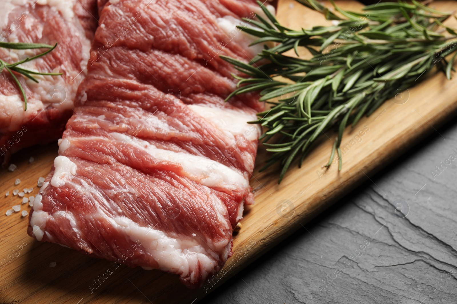 Photo of Raw ribs with rosemary and salt on black table, closeup