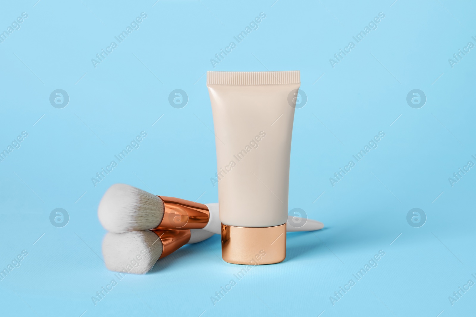 Photo of Tube of skin foundation and brushes on light blue background. Makeup product