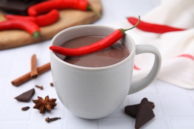 Cup of hot chocolate with chili pepper on white tiled table