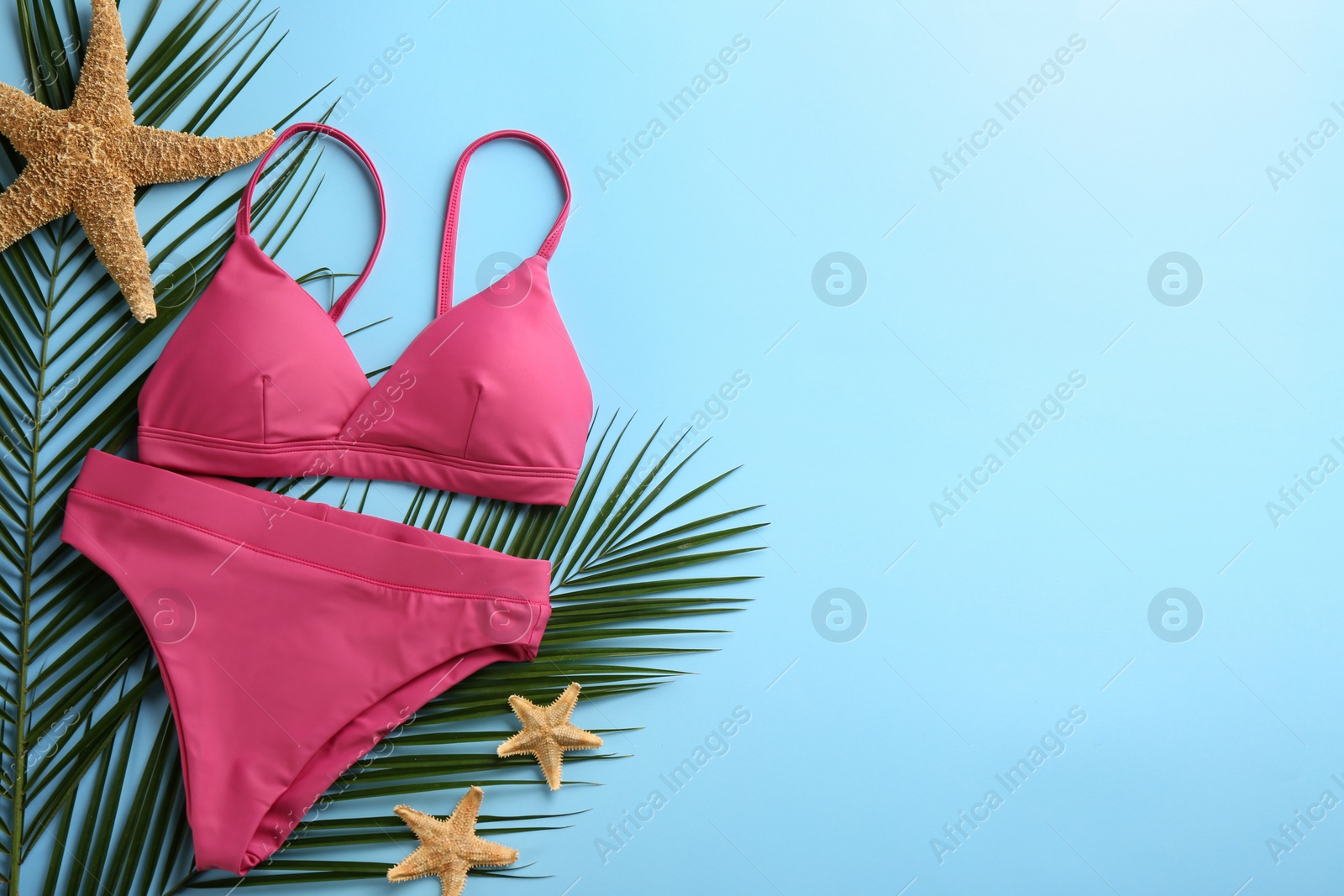 Photo of Beautiful pink bikini and beach accessories on light blue background, flat lay. Space for text