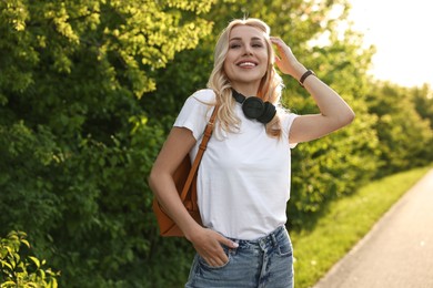 Happy young woman with headphones in park on spring day