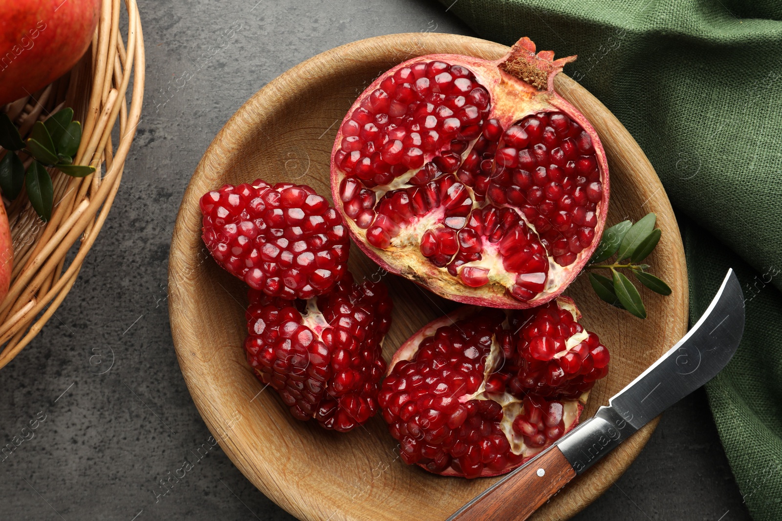 Photo of Fresh pomegranates, green leaves and knife on grey table, top view