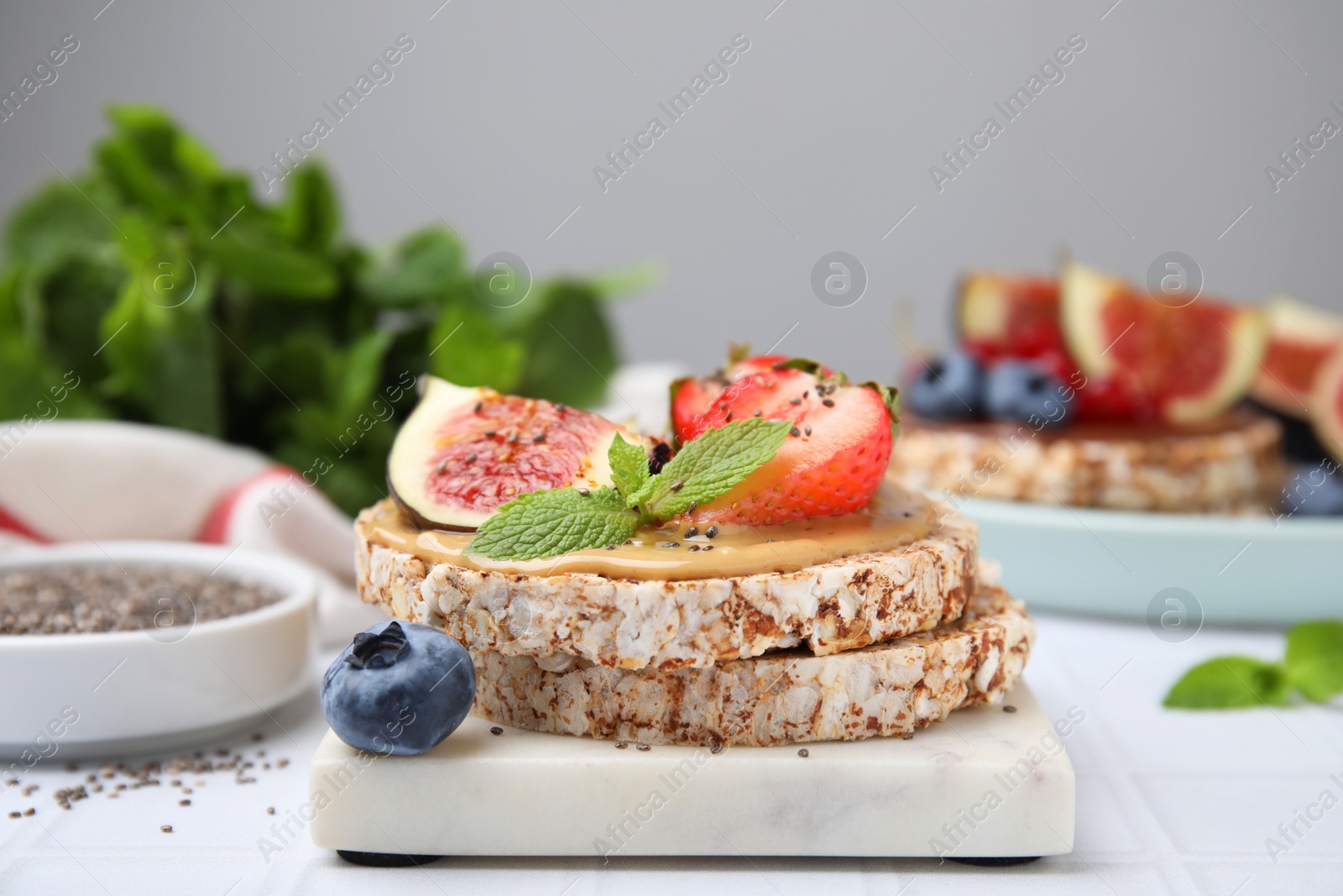 Photo of Tasty crispbreads with peanut butter, figs and berries on light table