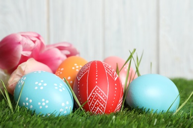 Photo of Colorful painted Easter eggs and spring flowers on green grass against wooden background