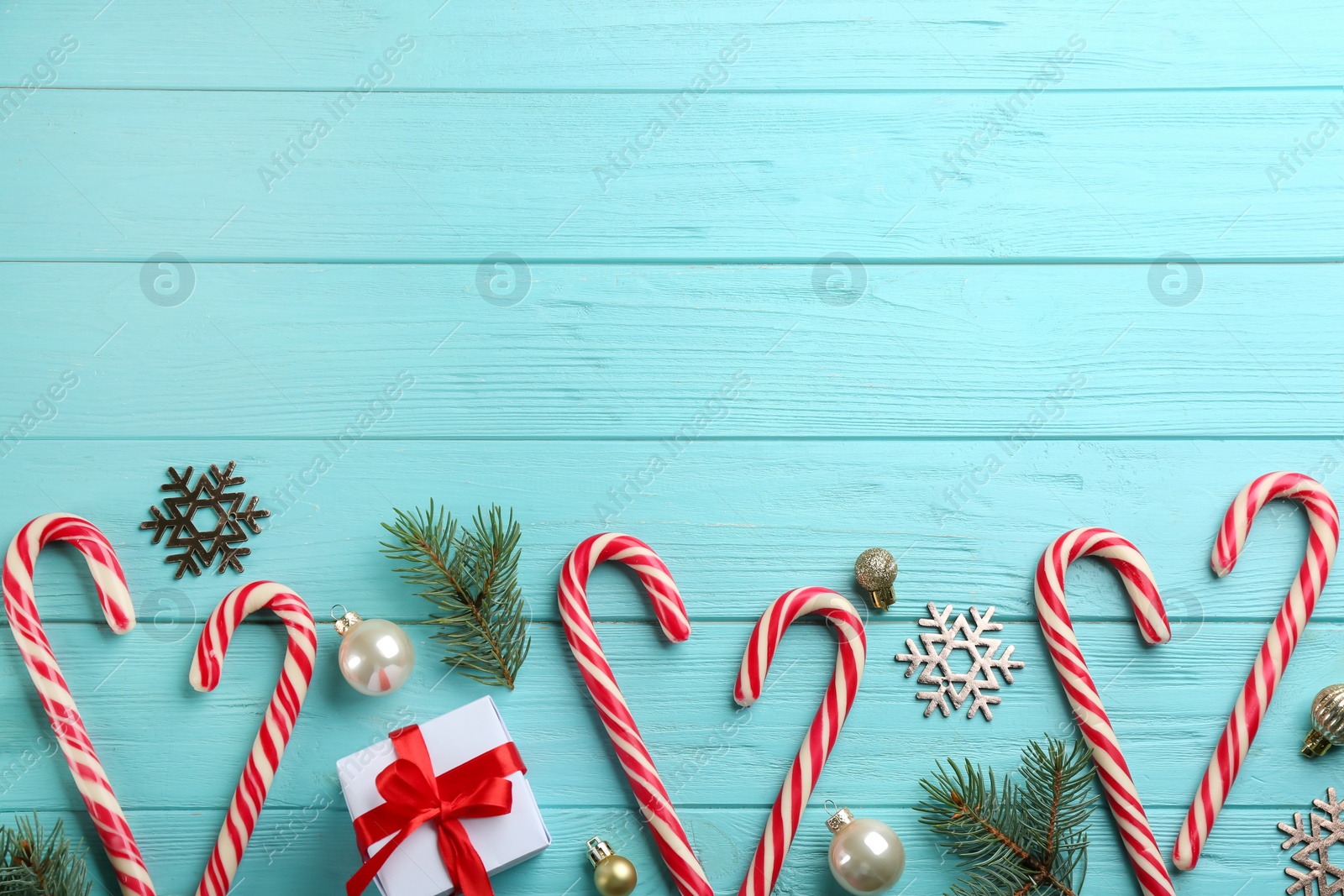 Photo of Flat lay composition with candy canes and Christmas decor on cyan wooden table. Space for text