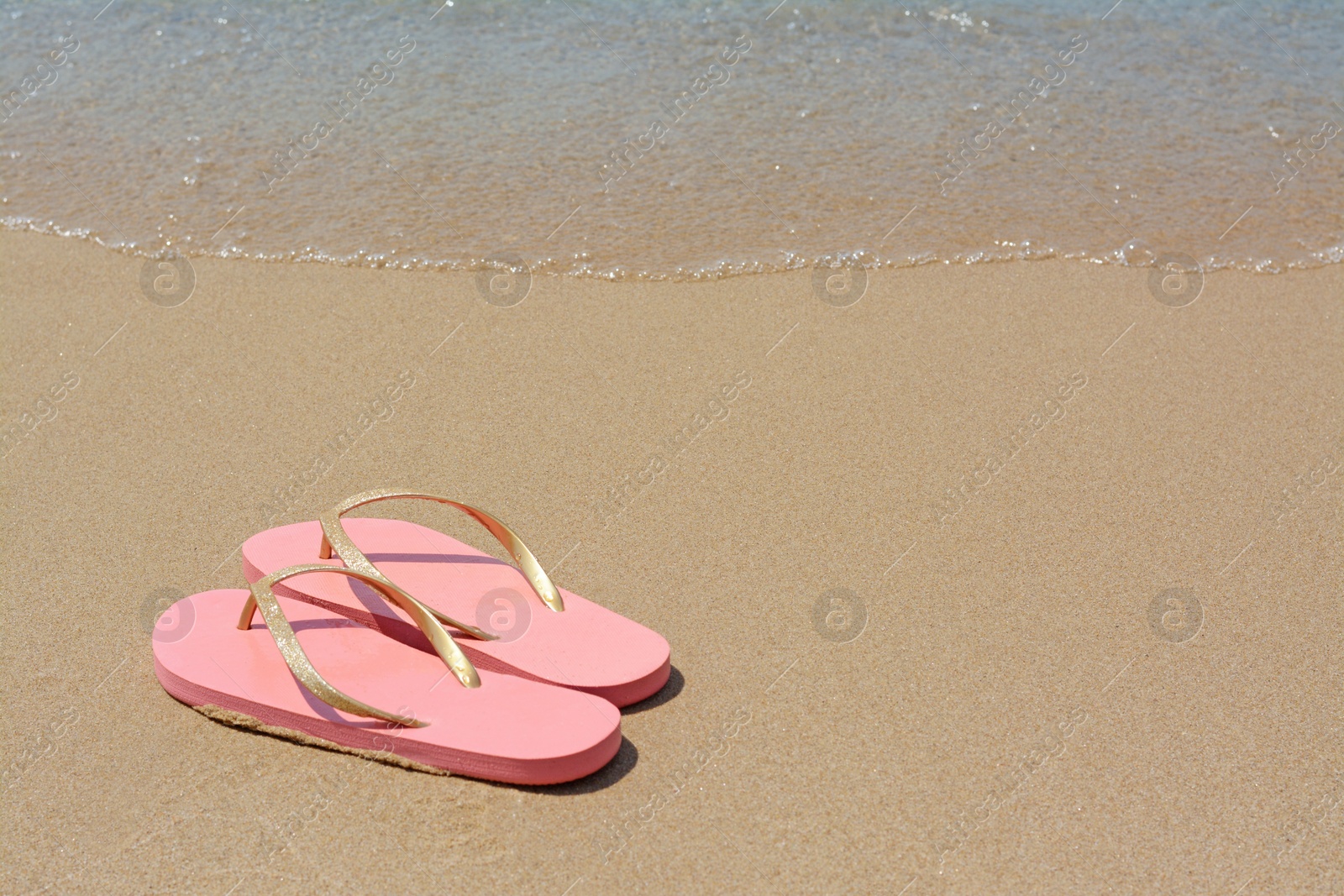 Photo of Stylish pink flip flops on wet sand near sea, space for text