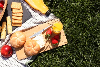 Picnic blanket with juice and snacks on green grass, flat lay. Space for text