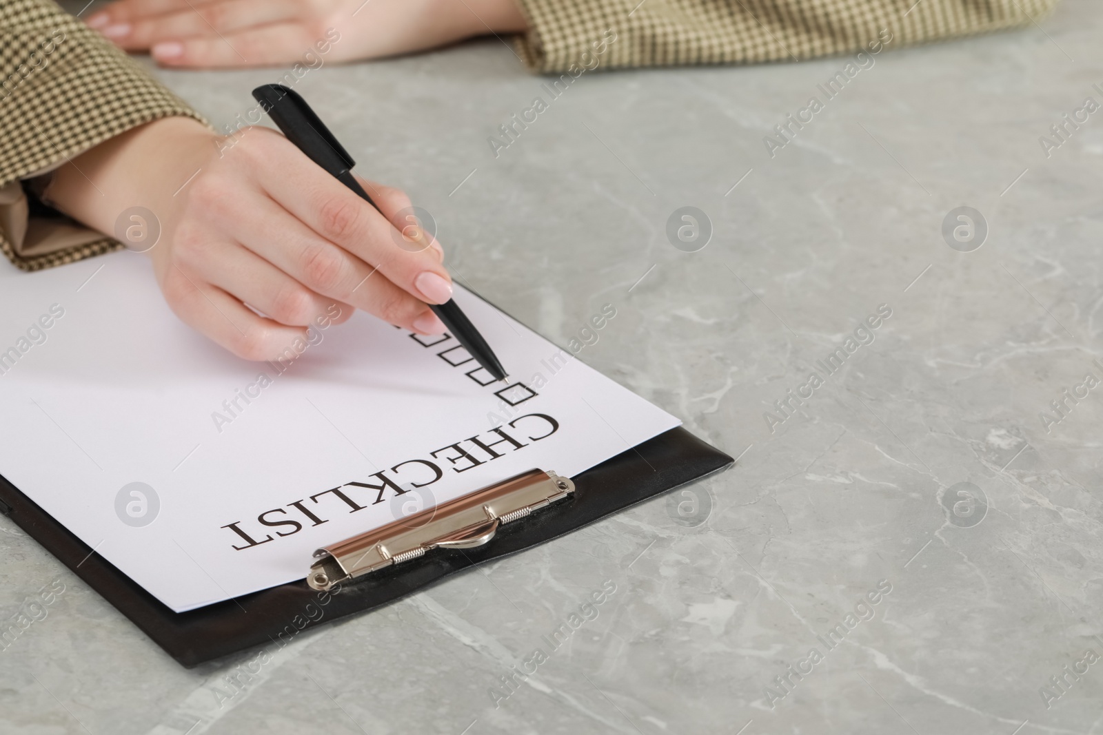 Photo of Woman filling Checklist at grey marble table, closeup. Space for text