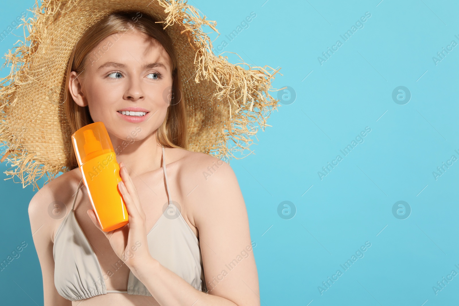 Photo of Beautiful young woman in straw hat with sun protection cream on light blue background, space for text