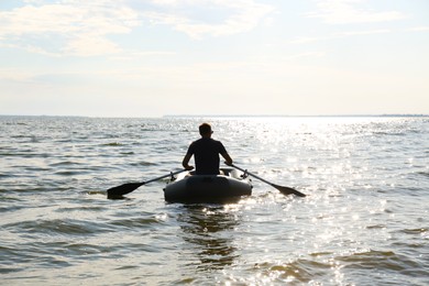 Man rowing inflatable rubber fishing boat on sea, back view