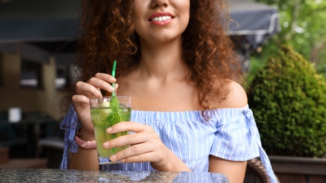 Happy African-American woman with glass of natural lemonade in cafe, closeup. Detox drink