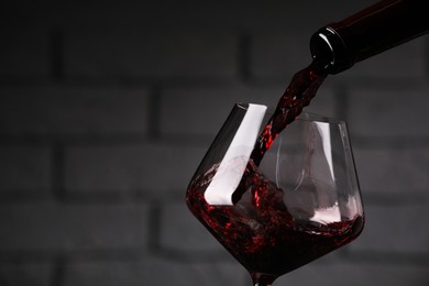 Photo of Pouring tasty red wine from bottle into glass against brick wall, closeup. Space for text