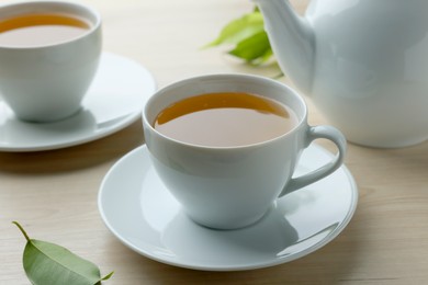 Photo of Green tea in white cups with leaves and teapot on wooden table, closeup