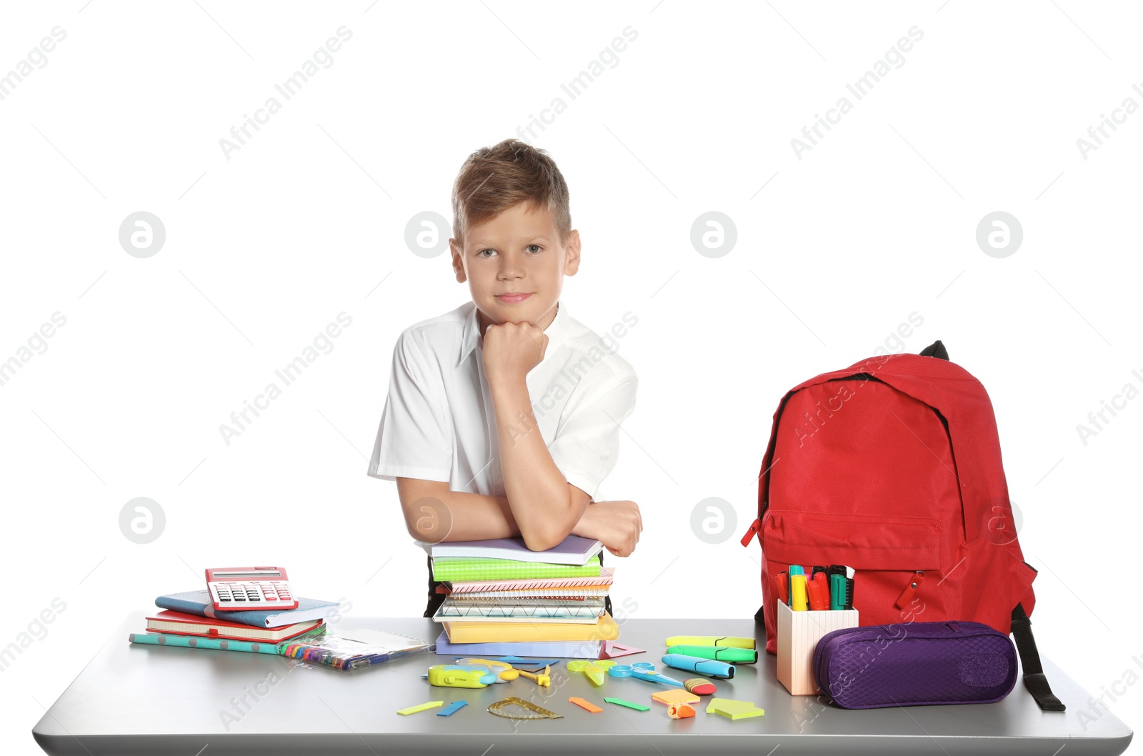 Photo of Cute boy sitting at table with school stationery against white background