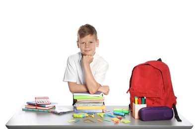 Cute boy sitting at table with school stationery against white background