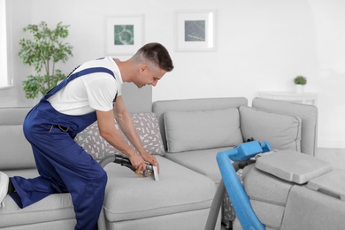 Photo of Dry cleaning worker removing dirt from sofa indoors