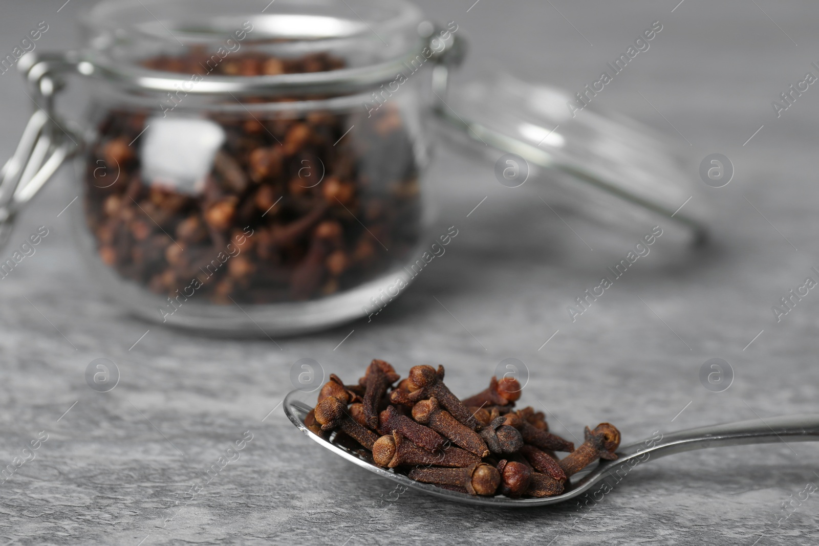 Photo of Spoon and jar with aromatic dry cloves on grey table