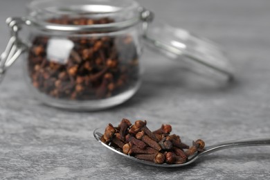 Photo of Spoon and jar with aromatic dry cloves on grey table