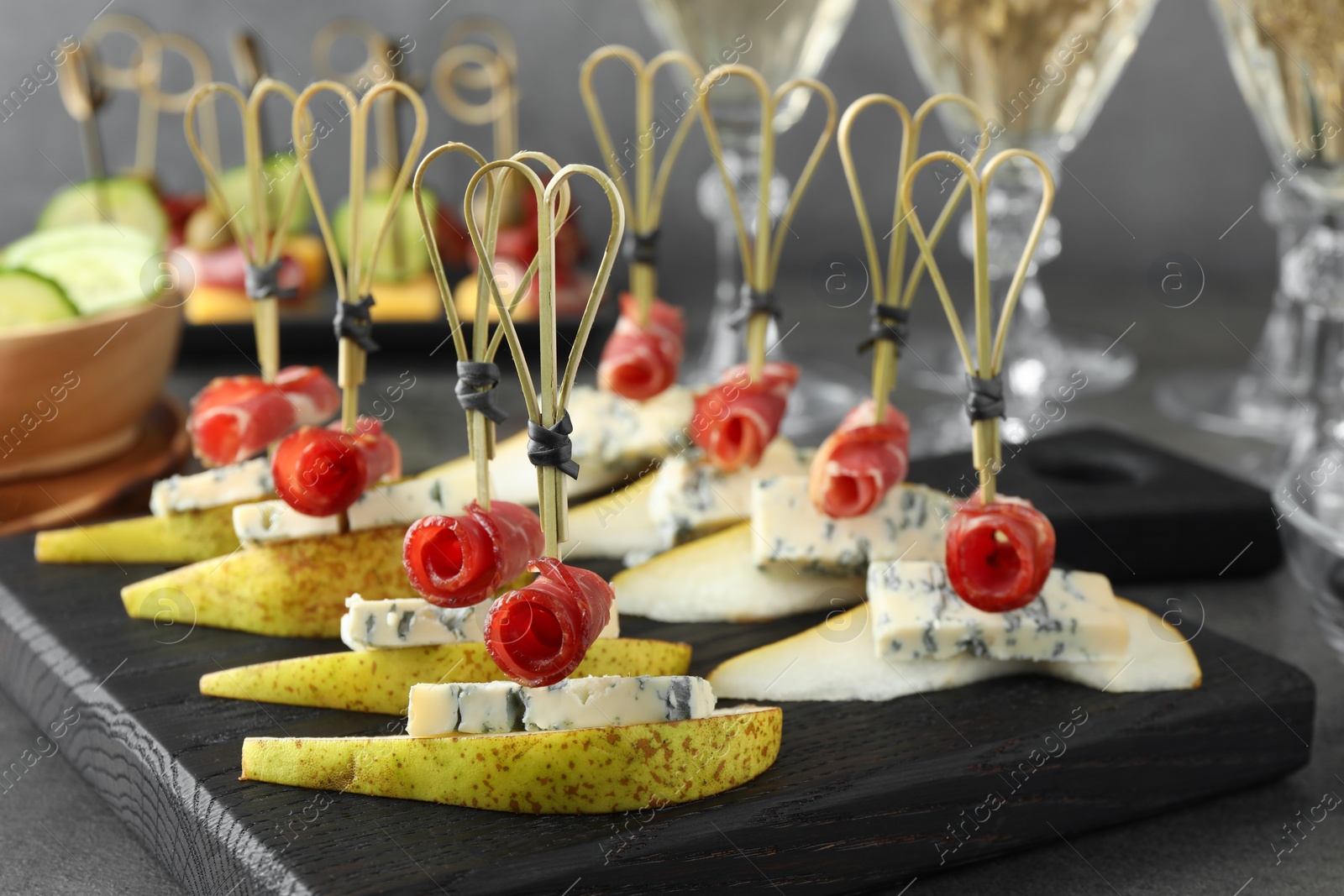 Photo of Tasty canapes with pears, blue cheese and prosciutto on grey table, closeup