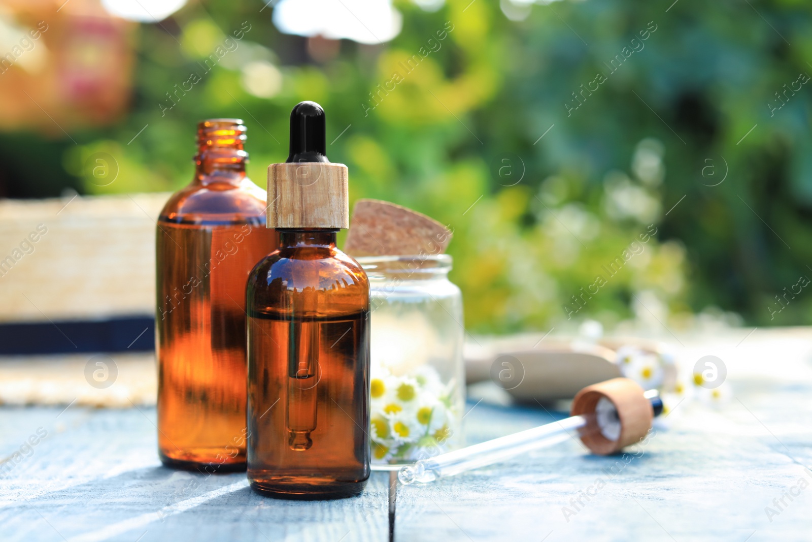 Photo of Bottles of essential oil, pipette and flowers on white wooden table, space for text