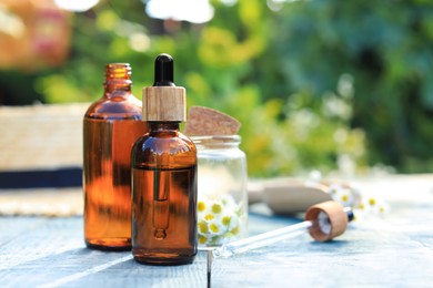 Bottles of essential oil, pipette and flowers on white wooden table, space for text