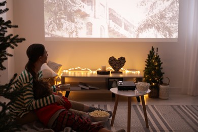 Mother and son watching Christmas movie via video projector at home