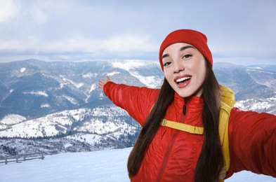 Happy tourist with backpack taking selfie in snowy mountains