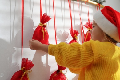 Photo of Little girl in Santa hat taking gift from Christmas advent calendar indoors, closeup
