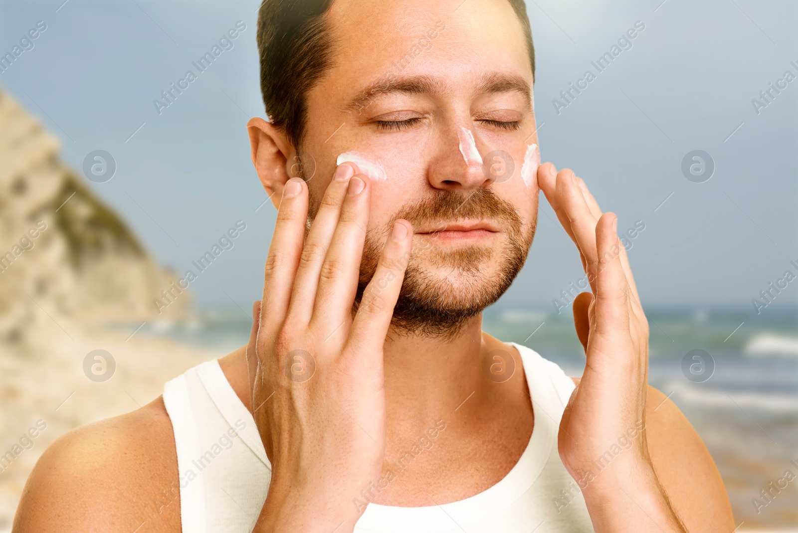 Image of Sun protection. Man applying sunblock onto face on beach