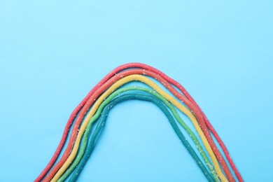 Rainbow of gummy strings on light blue background, flat lay