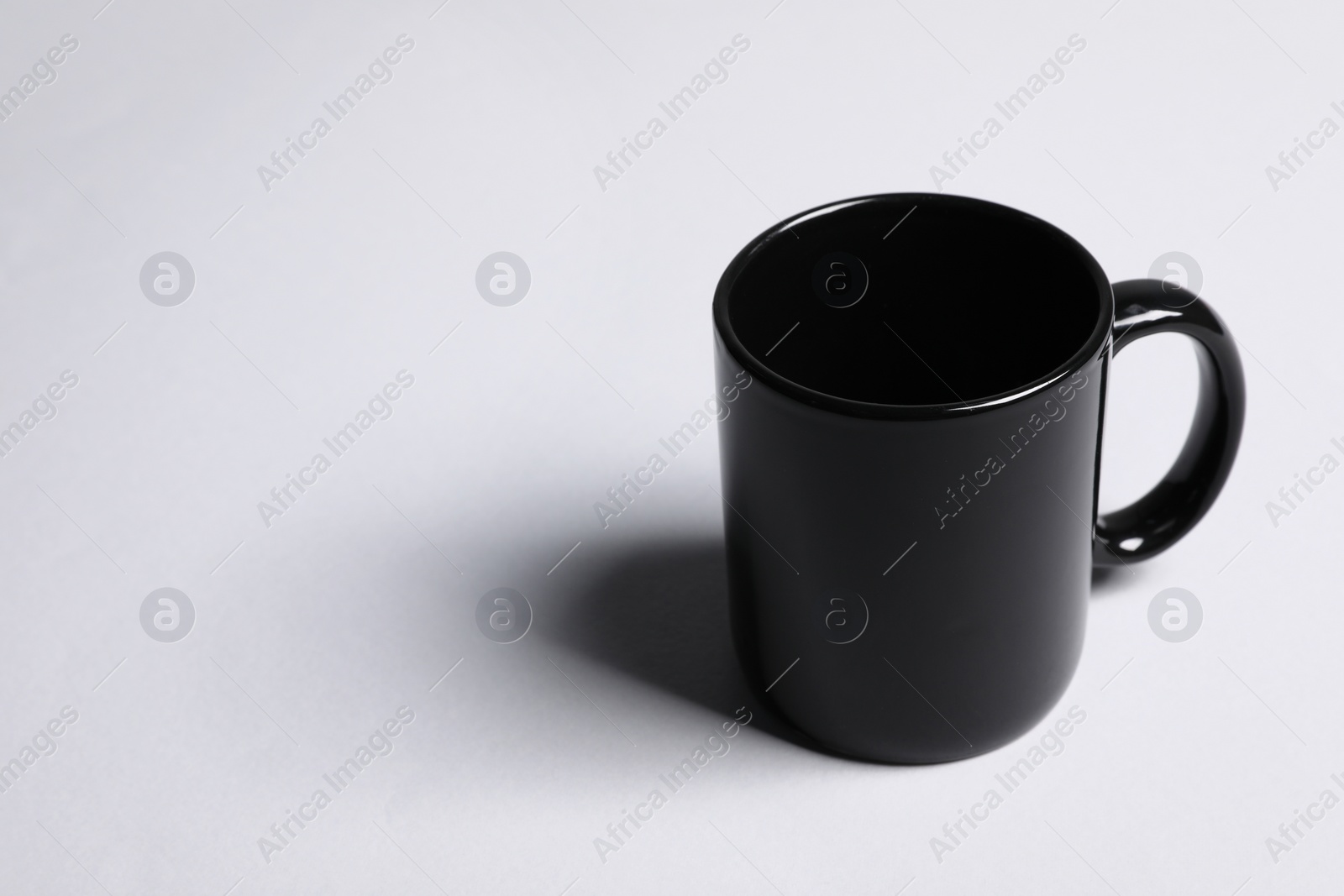 One black ceramic mug on light grey background, space for text Photo of One black ceramic mug on light grey background, space for text