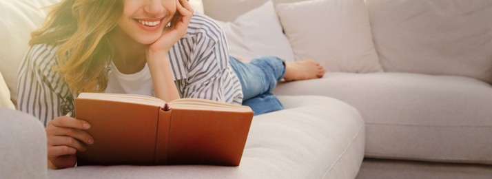 Young woman reading book on sofa at home, space for text. Banner design