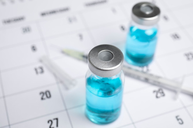 Photo of Vial and syringe on calendar, closeup. Vaccination and immunization