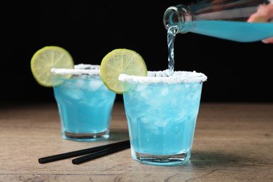 Photo of Bartender making cocktail with light blue drink at wooden table, closeup