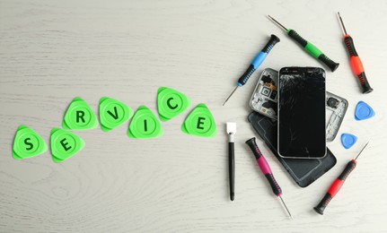 Damaged smartphone and repair tools on white wooden background, flat lay