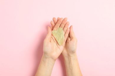 Woman with jade gua sha tool on light pink background, closeup
