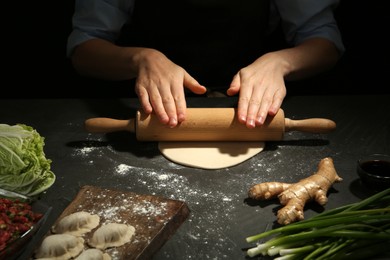 Woman rolling dough for gyoza at grey table, closeup