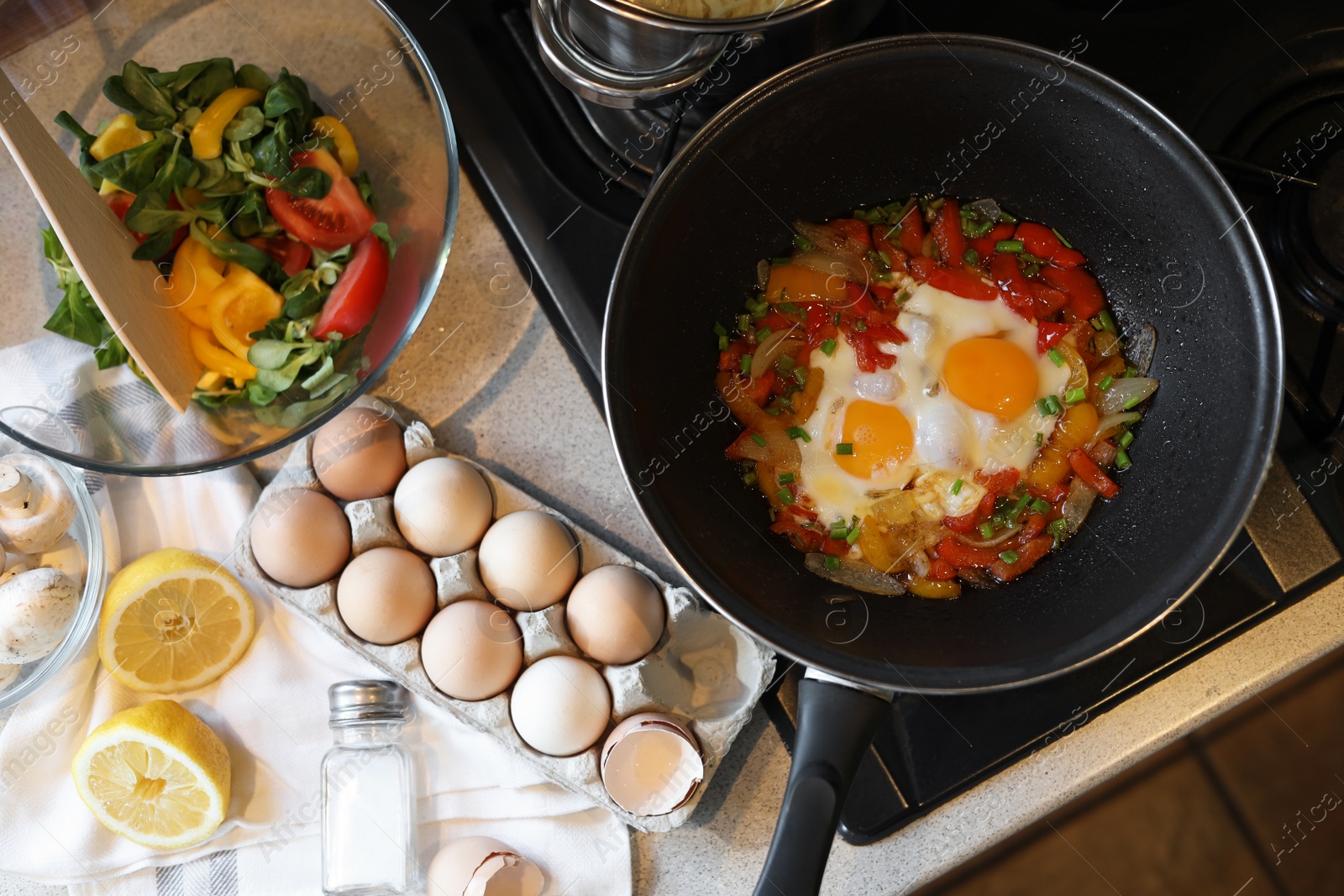 Photo of Frying pan with tasty eggs and vegetables near products on kitchen counter, top view