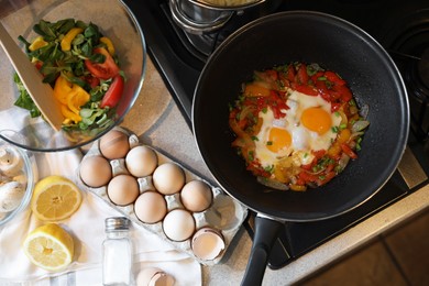 Frying pan with tasty eggs and vegetables near products on kitchen counter, top view