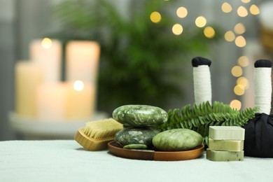 Spa composition. Herbal massage bags, stones and soap bars on white towel against blurred background. Space for text