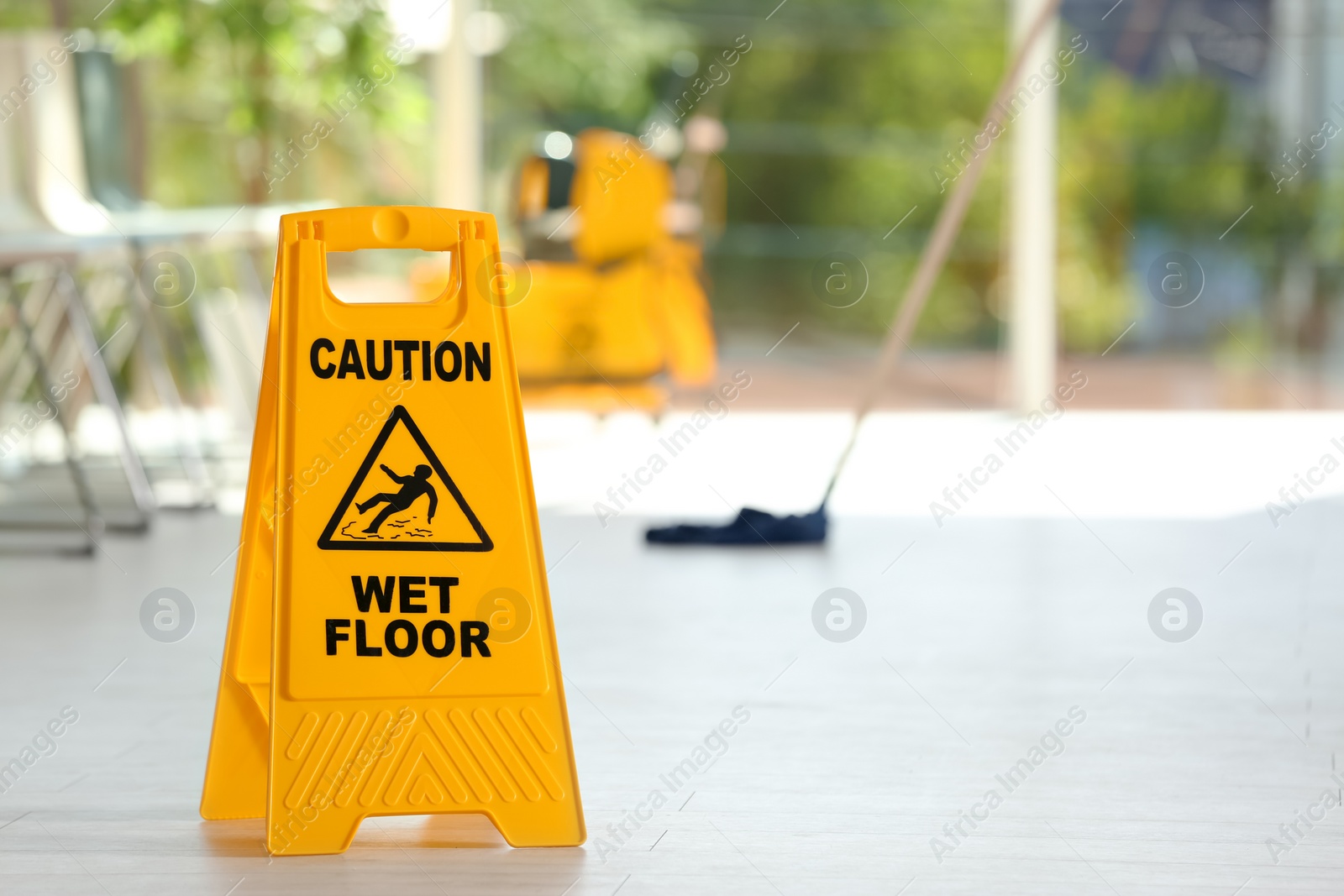 Photo of Safety sign with phrase Caution wet floor and blurred mop bucket on background. Cleaning service