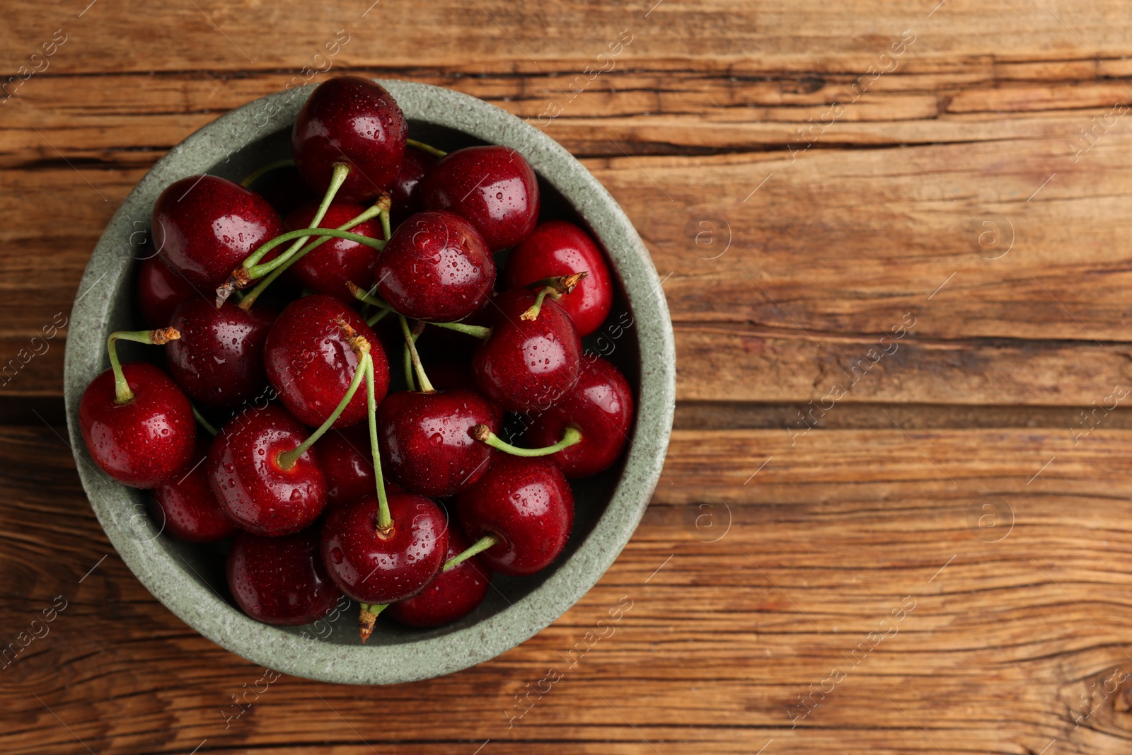 Photo of Bowl with ripe sweet cherries on wooden table, top view. Space for text