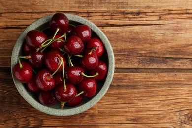 Bowl with ripe sweet cherries on wooden table, top view. Space for text