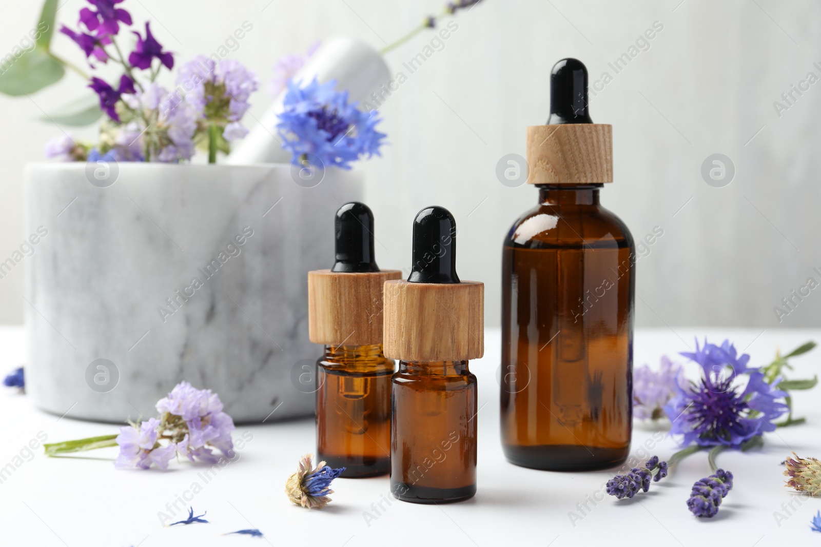 Photo of Aromatherapy. Essential oils, flowers, mortar and pestle on white table