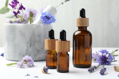 Aromatherapy. Essential oils, flowers, mortar and pestle on white table