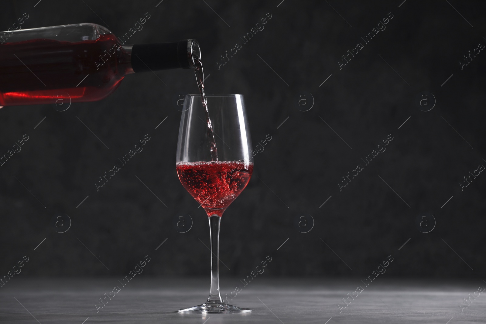 Photo of Pouring red wine from bottle into glass on table, space for text