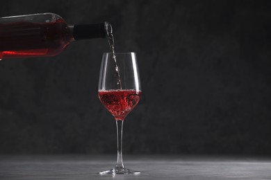 Photo of Pouring red wine from bottle into glass on table, space for text