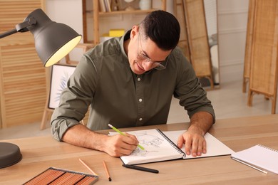 Photo of Man drawing in sketchbook with pencil at wooden table indoors